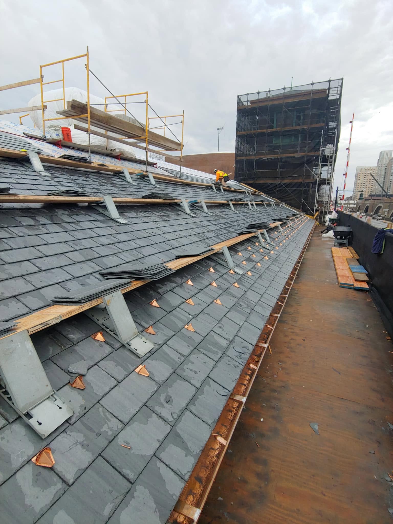 Roofing construction site with workers installing slate tiles and safety scaffolding on urban building