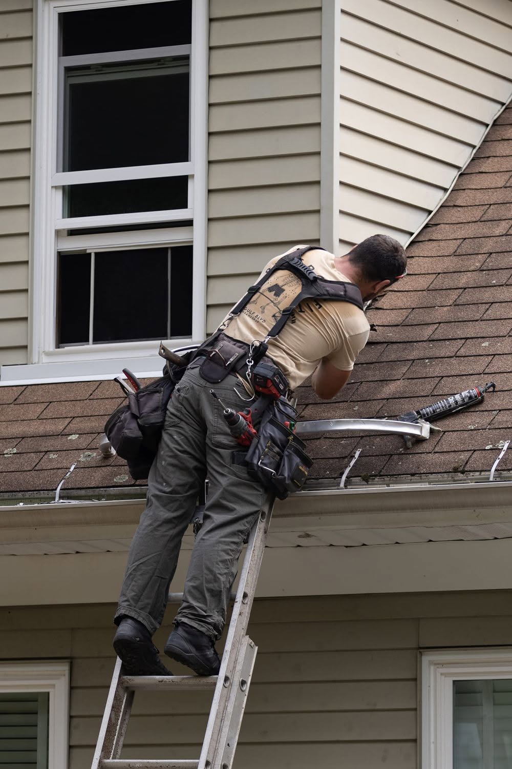 Professional contractor on ladder installing gutter system on residential home exterior