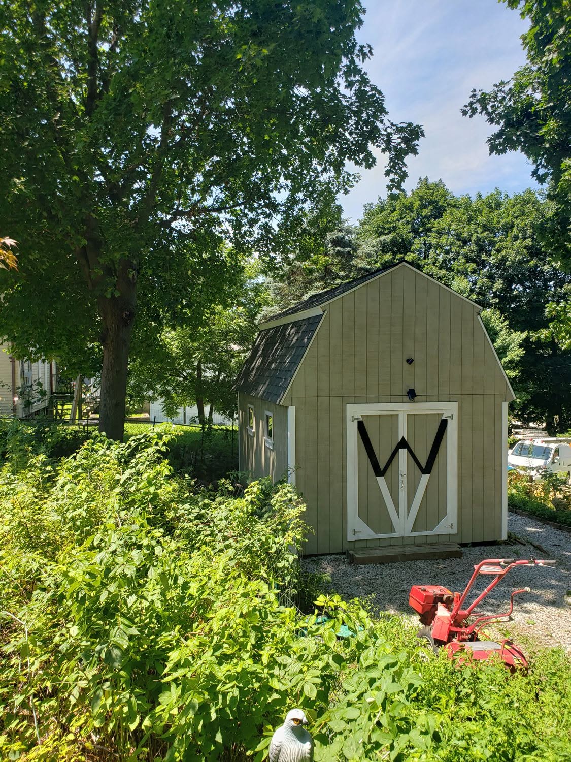 Sage green garden shed with white barn doors in residential backyard surrounded by trees
